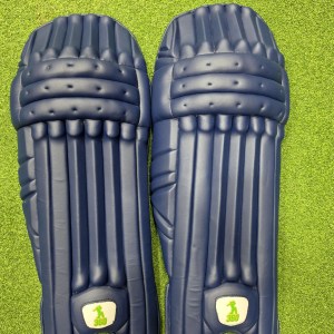 Top view of EM 360 Bull Ring adult navy blue cricket batting pads on artificial grass on Alberta.